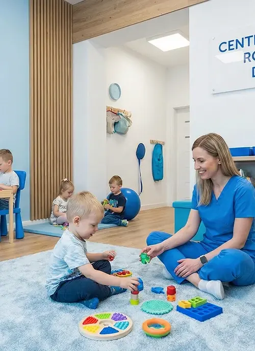 Terapeutka prowadzi zajęcia sensoryczne z grupą małych dzieci na dywanie